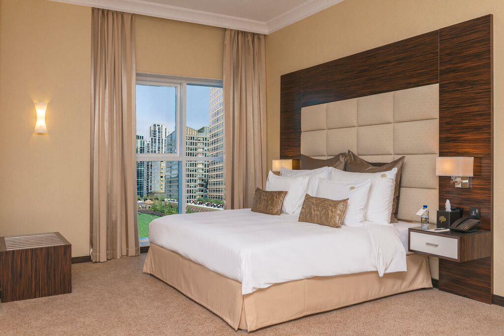Hotel Jannah Burj Al Sarab Abu Dabi Exterior foto The photo shows a well-decorated hotel room featuring a large bed with white bedding and decorative pillows. The walls are painted in a warm color, and there are modern wooden accents. On one side, there are light fixtures, and beside the bed, there 
